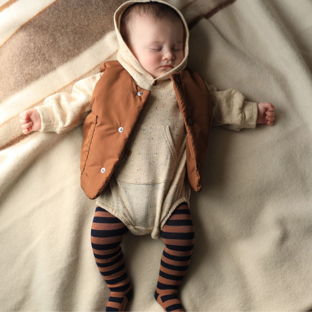 Baby wearing a brown vest and striped leggings lying on a soft surface