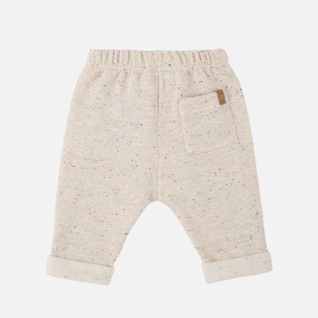 Sold at Bombon shop, designed by 1+ in the family — oatmeal-colored baby pants with multicolor speckles, contrast drawstring, and rolled cuffs, photographed flat on white background. back