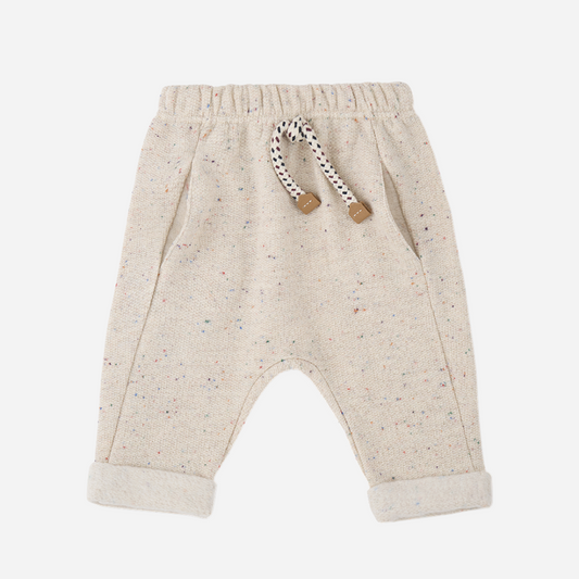 Sold at Bombon shop, designed by 1+ in the family — oatmeal-colored baby pants with multicolor speckles, contrast drawstring, and rolled cuffs, photographed flat on white background. front