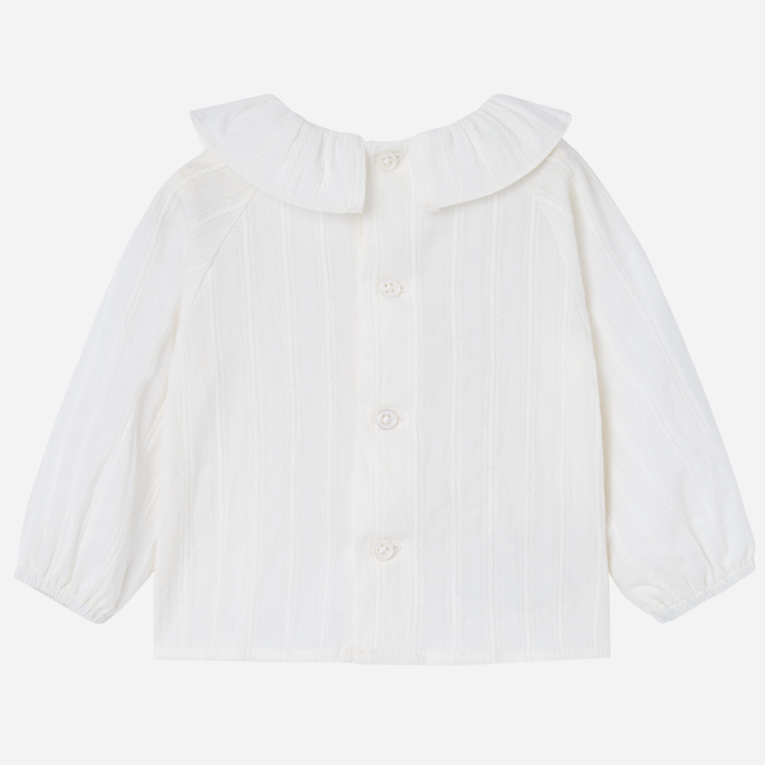 Sold at Bombon shop, designed by Paz Rodriguez, white baby blouse with ruffled collar and puffed sleeves.