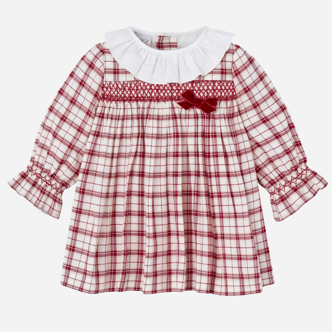 Sold at Bombon shop, designed by Paz Rodriguez, baby holiday dress in red plaid with smocking, white ruffle collar, and velvet bow.