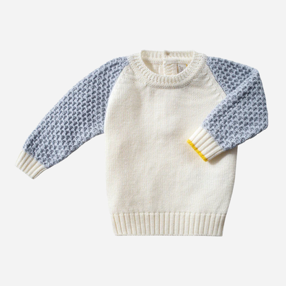 Sold at Bombon and designed by Gensami, a baby knit set including an ivory sweater with blue textured sleeves and matching ivory pants, both detailed with yellow trim accents.