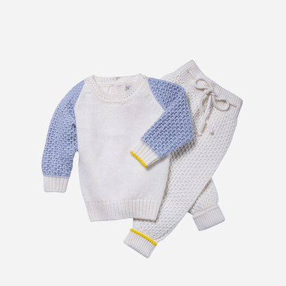 Sold at Bombon and designed by Gensami, a baby knit set including an ivory sweater with blue textured sleeves and matching ivory pants, both detailed with yellow trim accents.