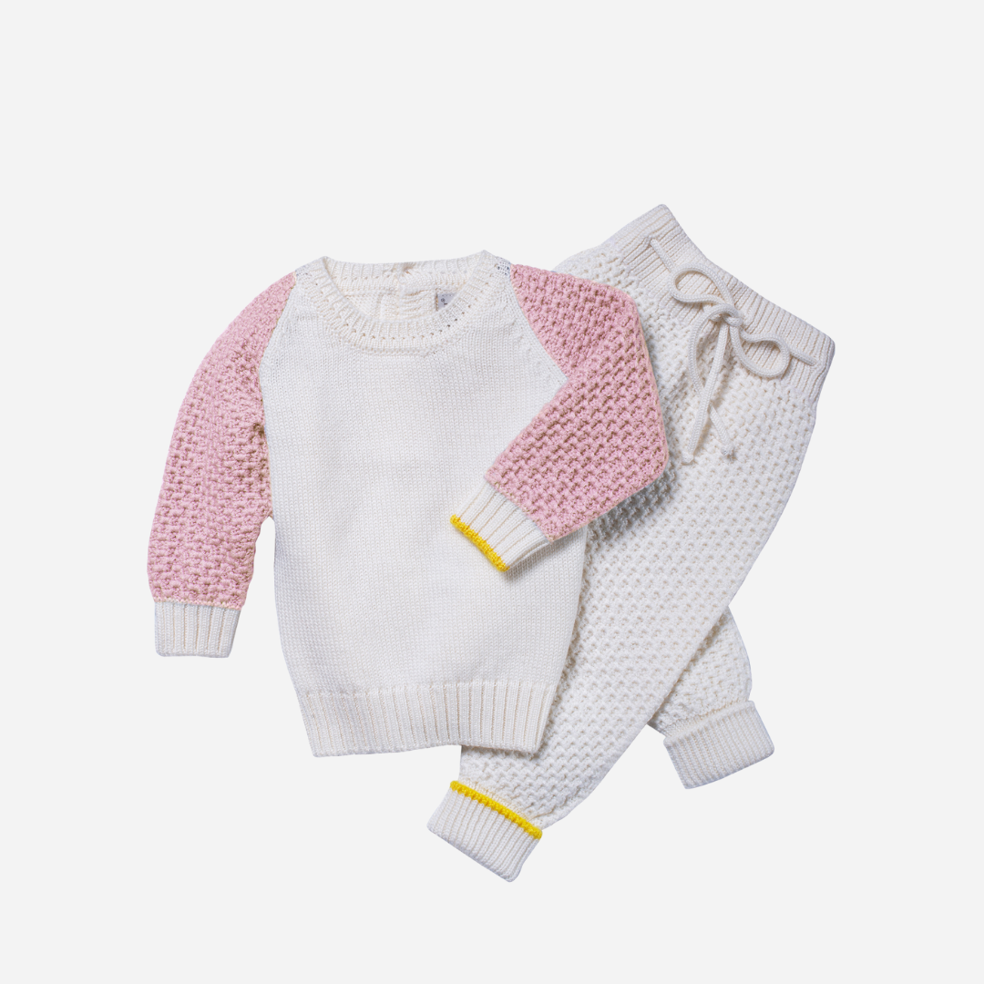 Sold at Bombon and designed by Gensami, a soft pink knit baby romper featuring front buttons, white ribbed cuffs, a bear motif on the chest pocket, and a yellow trim detail on the sleeve.