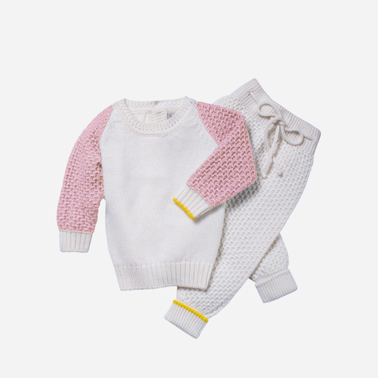 Sold at Bombon and designed by Gensami, a soft pink knit baby romper featuring front buttons, white ribbed cuffs, a bear motif on the chest pocket, and a yellow trim detail on the sleeve.
