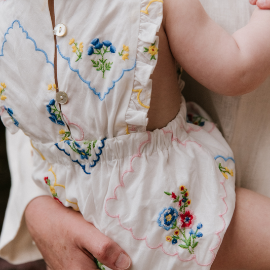 sold at Bombon, designed by The New Society baby romper with multicolor floral embroidery on soft cotton with ruffle details matching sibling set