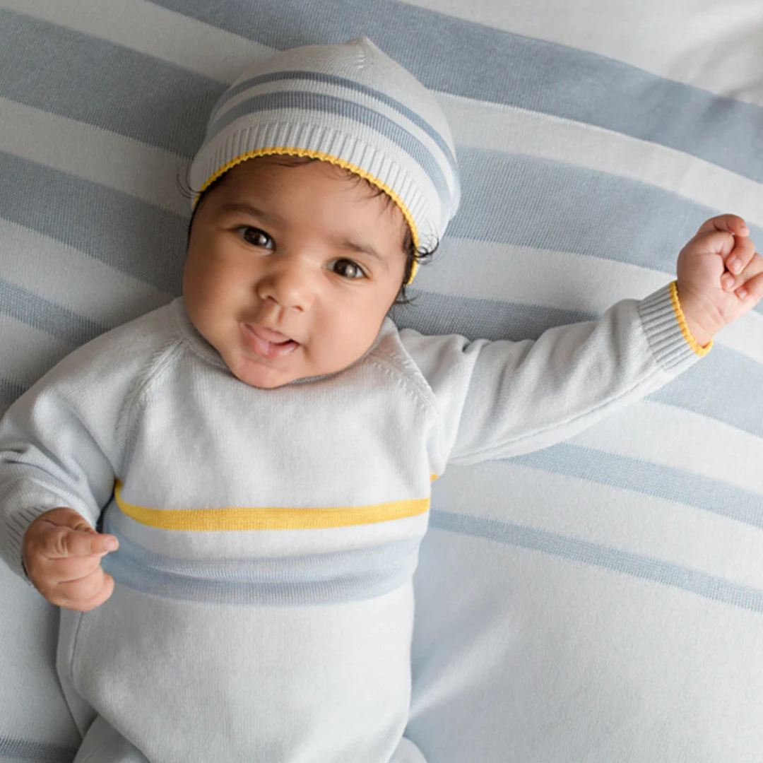 Sold at Bombon and designed by Gensami, a blue newborn layette set including a knit jumpsuit, hat, socks, and matching blanket with yellow stripe detailing.