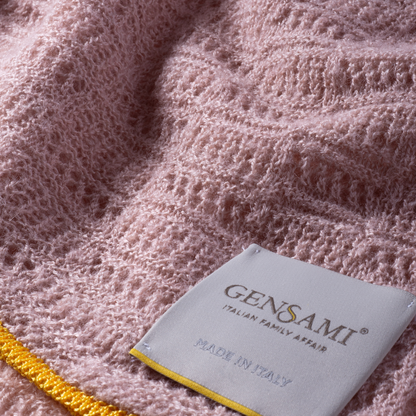 Sold at Bombon and designed by Gensami, a pink knitted baby blanket with openwork texture and a contrasting yellow trim along the border.