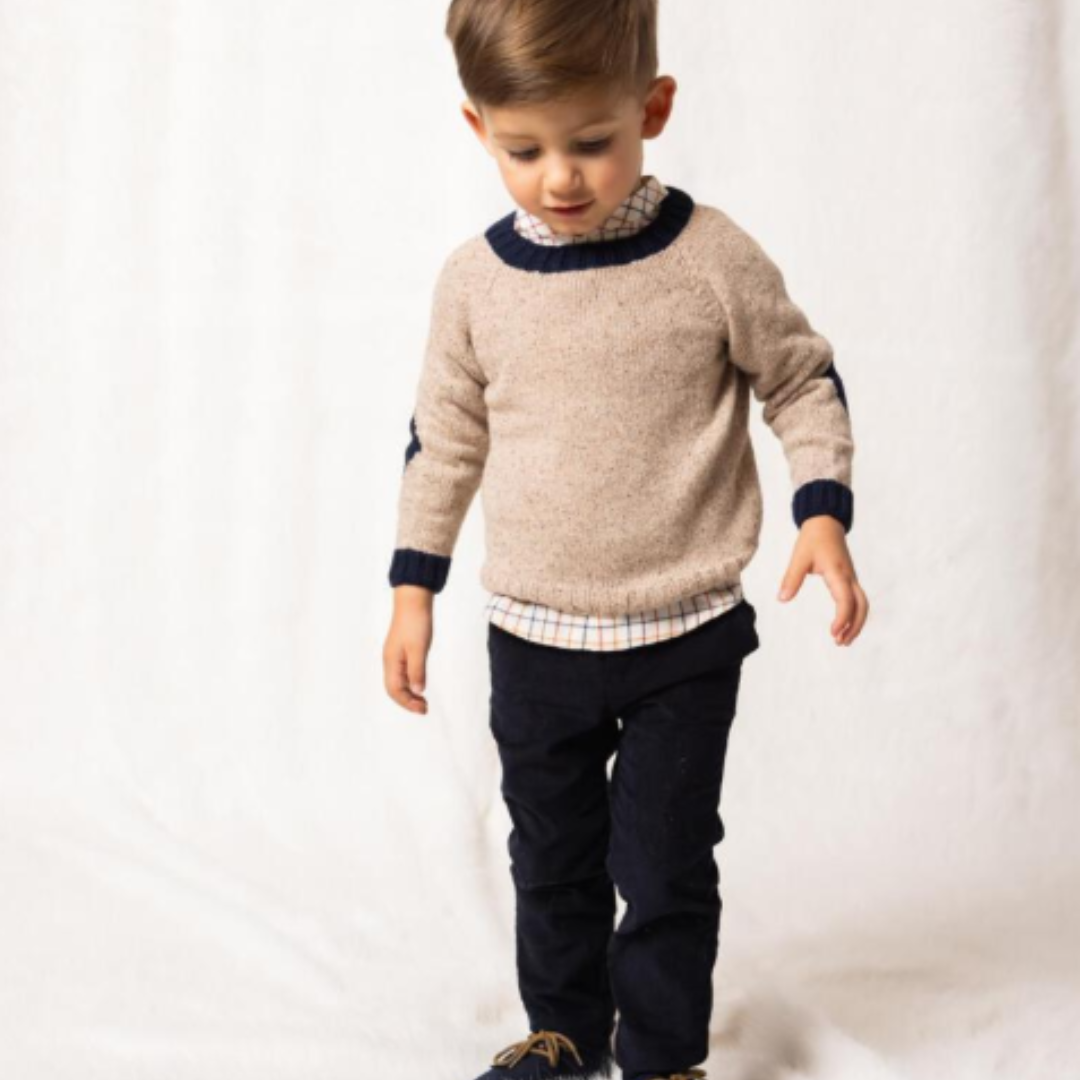 Sold at Bombon shop, designed by Fina Ejerique, a beige knit baby sweater with navy ribbed collar and cuffs, styled to pair with the multicolor checkered shirt. model