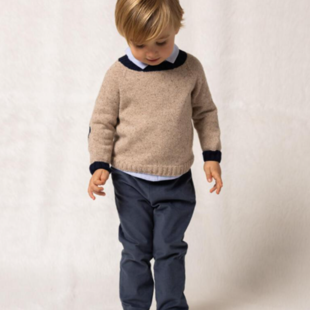 Sold at Bombon shop, designed by Fina Ejerique, a beige knit baby sweater with navy ribbed collar and cuffs, styled to pair with the multicolor checkered shirt. model